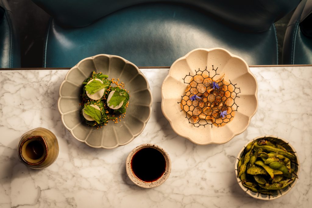 Overhead view of Japanese small plates at Aki London in Marylebone, including edamame, seasonal vegetables and dipping sauce on a marble table, perfect for your next Instagram story