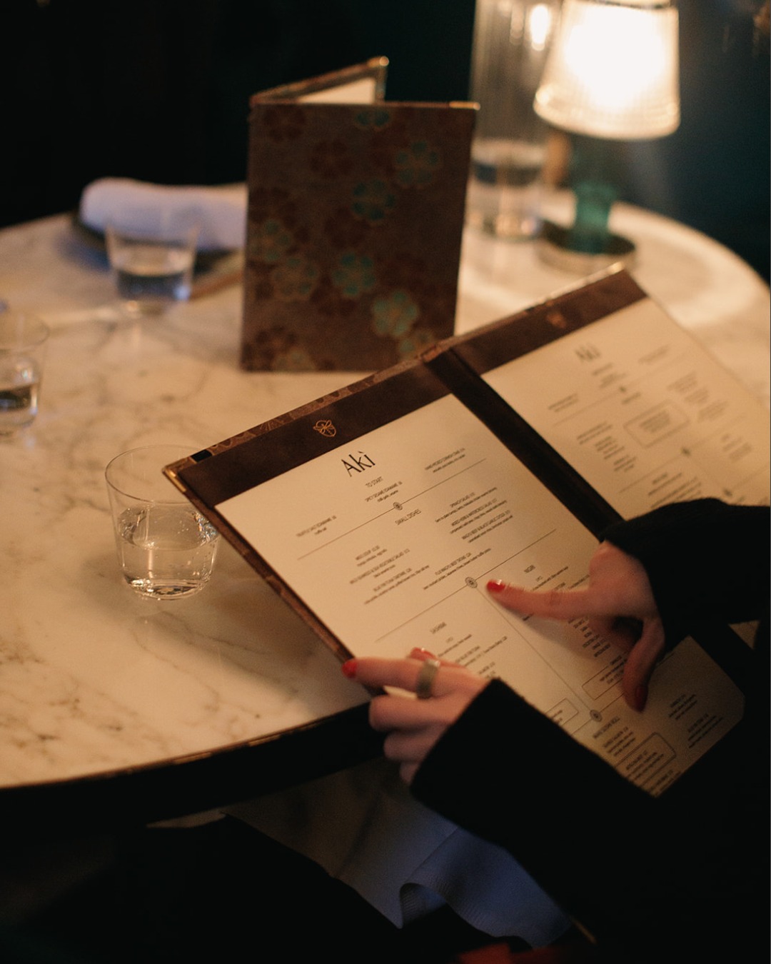Guest reading the Aki menu on a marble table at a Japanese date night restaurant in Marylebone, London